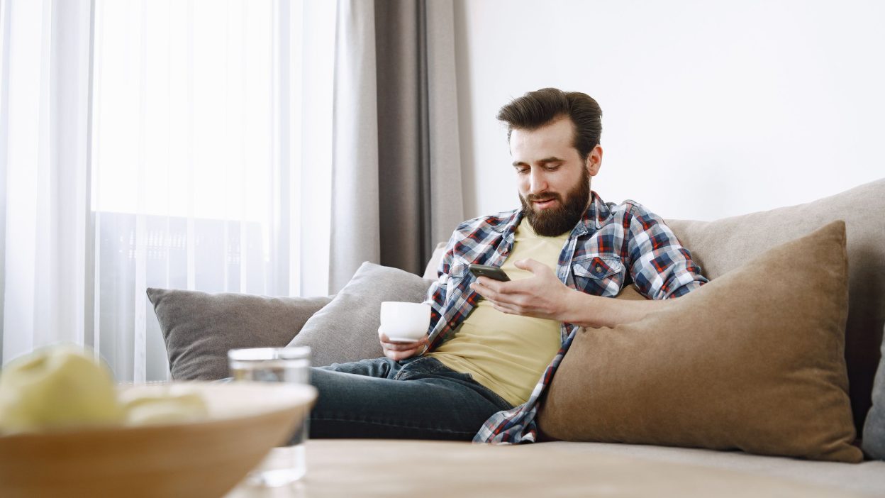 Hombre en el sofá respondiendo una encuesta de Ipsos iSay en el móvil