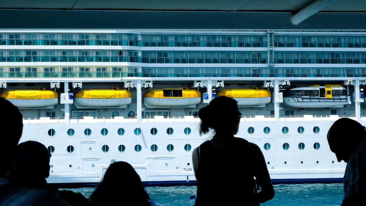 Personas mirando un gran crucero en el puerto, donde se puede trabajar a bordo